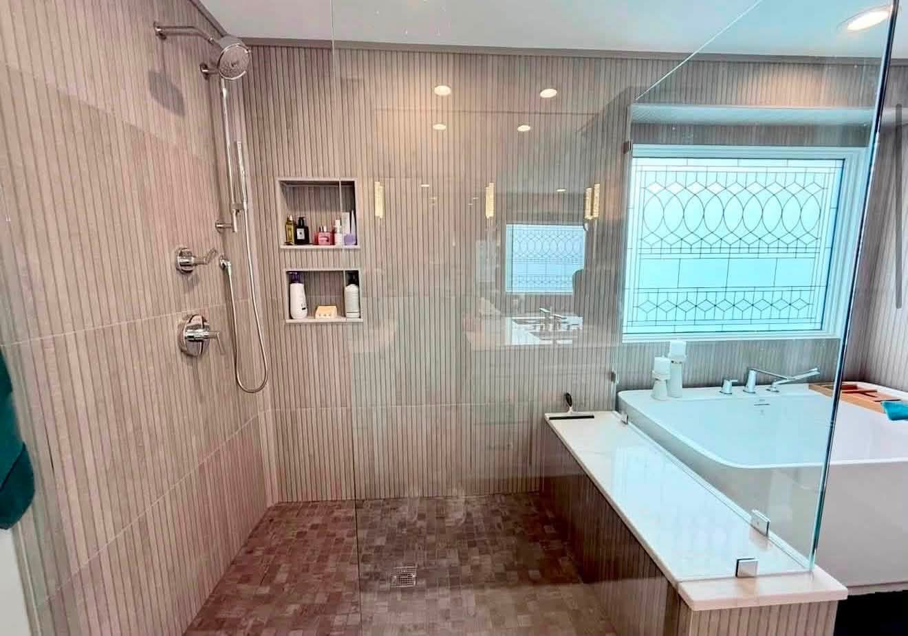 After: serene shower with vertical tile, glass enclosure and built-in niche