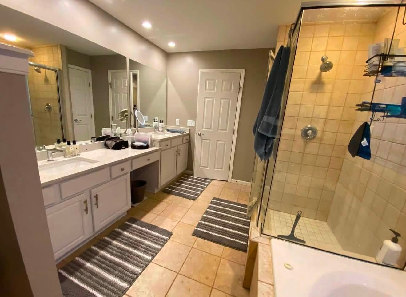 Primary bathroom before: double vanity, tan tile floor and dated shower enclosure
