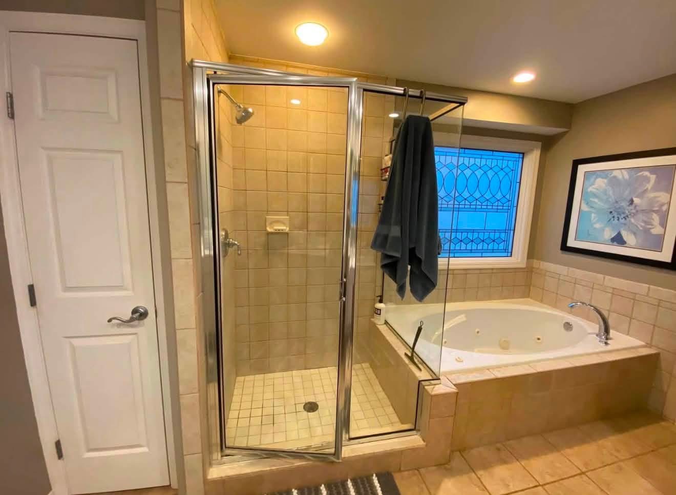 Before: framed shower door beside a tiled soaking tub surround